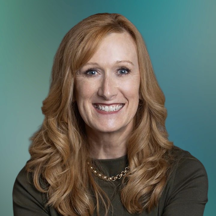 A portrait headshot of a white woman with dark blond hair wearing a green blouse and a fine gold chain necklace, smiling