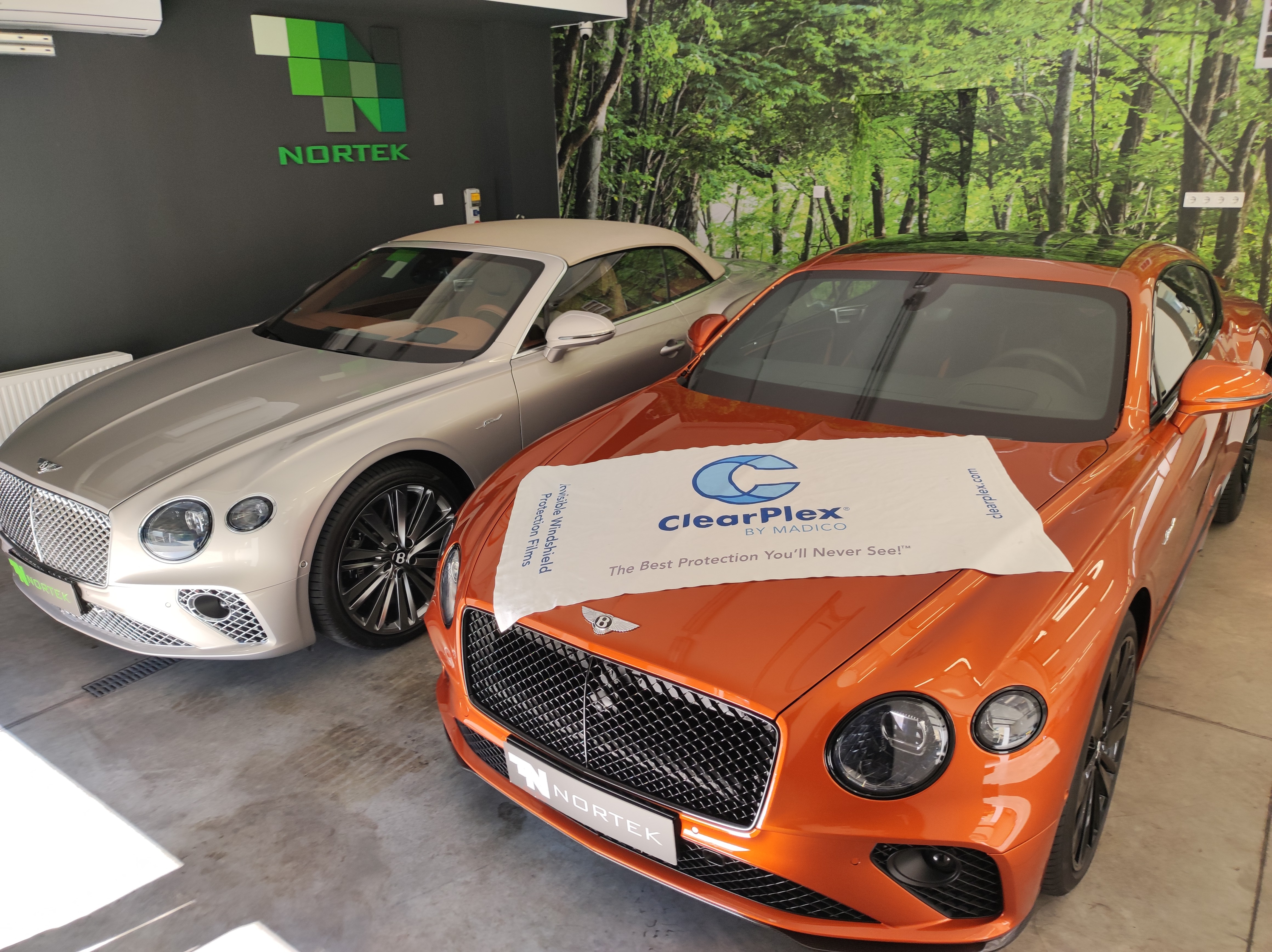 Kavicsfelverődés elleni ClearPlex láthatatlan szélvédővédő fóliázásra váró narancssárga és ezüst Bentley luxusautók a Nortek budapesti műhelyében.
