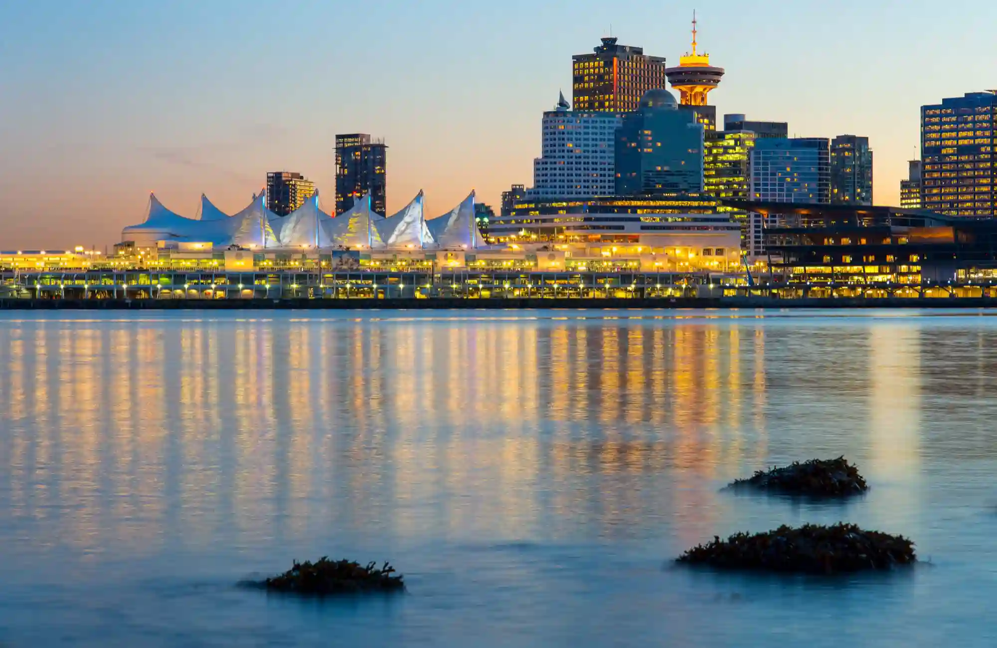 A twilight photo of the Vancouver skyline from the water, featuring Canada Place and the Harbour Centre tower.