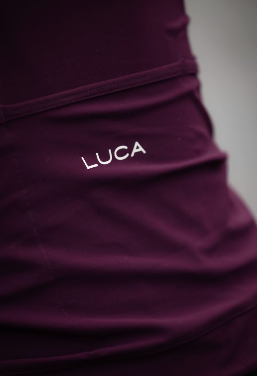 Close-up-of-the-back-pocket-area- of-a-dark-purple-cycling-jersey- showing-the-white-embroidered- printed-LUCA-brand-logo