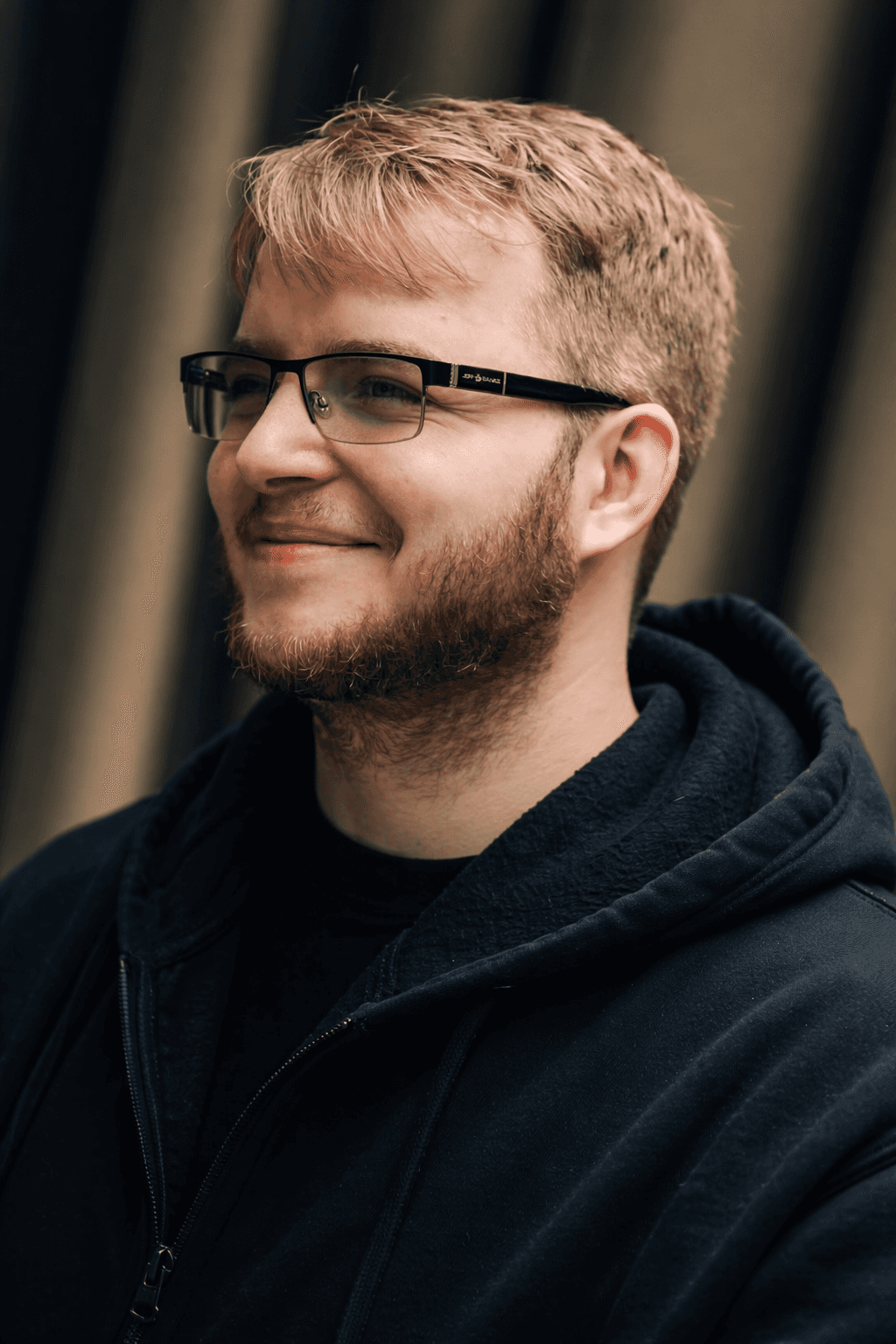 Portrait of a woman with long, smooth hair swept to the side, in a dark t-shirt, on a plain background.