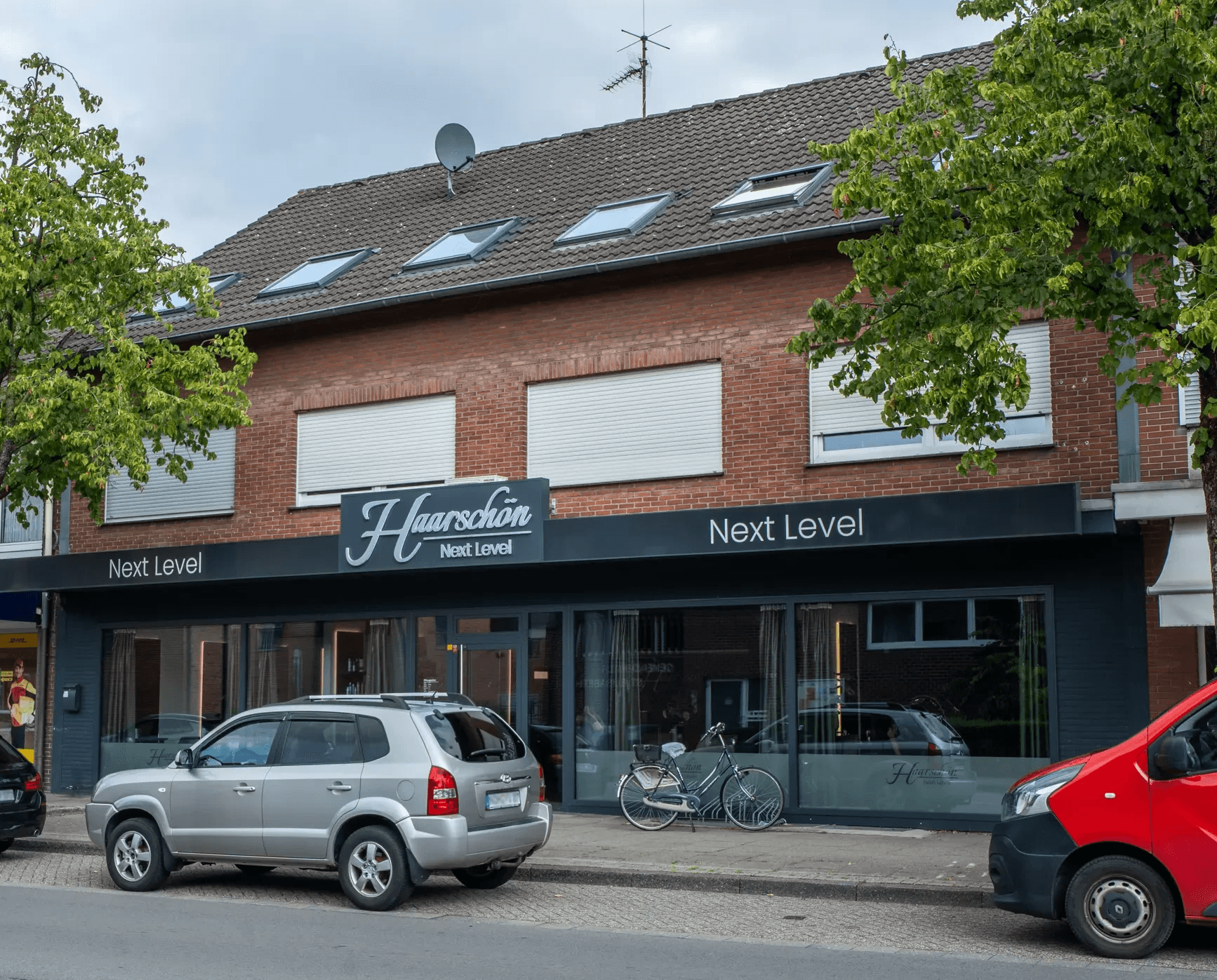 Straßenansicht eines Wohn- und Geschäftshauses mit Dachgeschosswohnung, mehreren Dachfenstern und Friseursalon im Erdgeschoss.