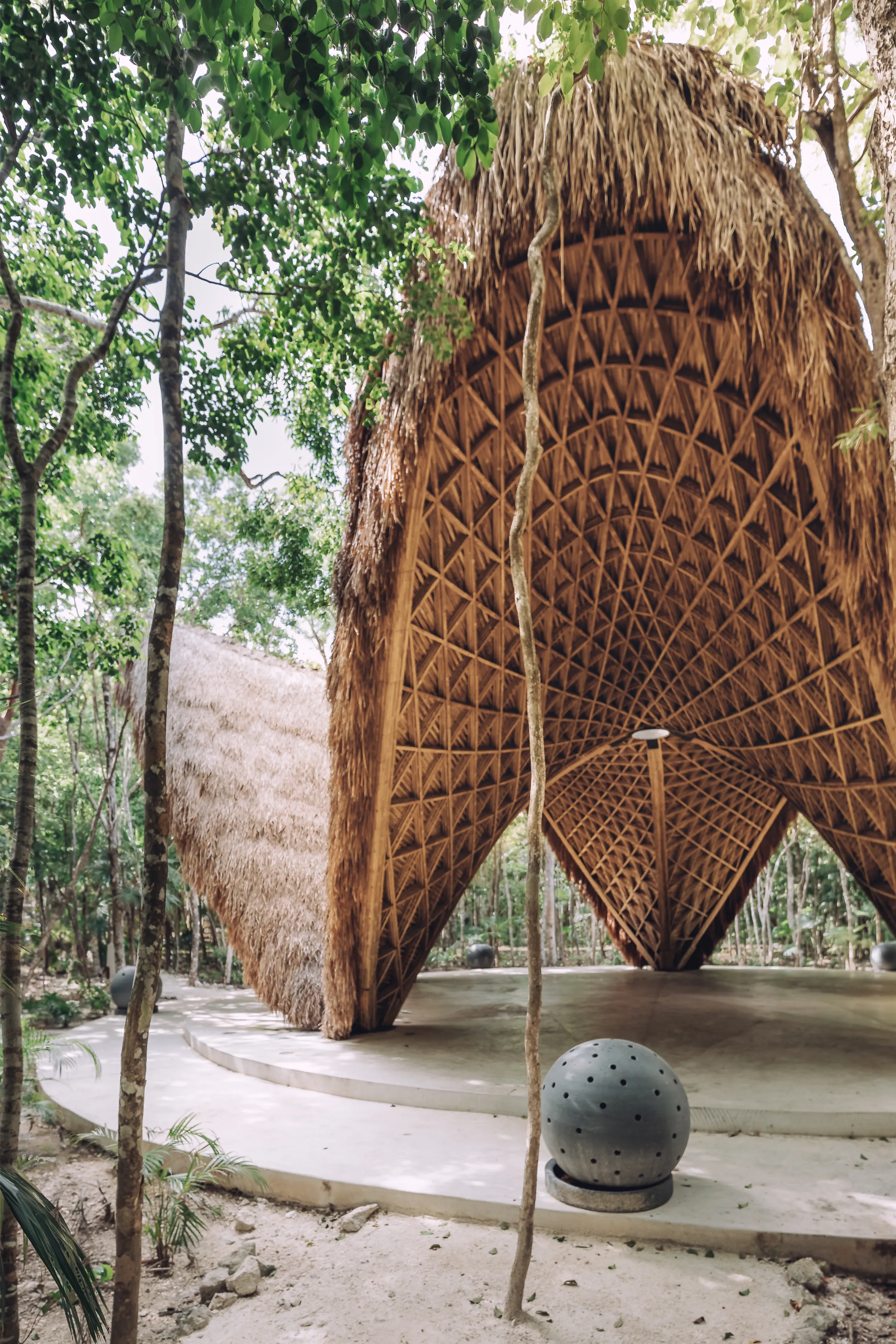 Vertical perspective of the Luum Temple entrance in Tulum, showing the impressive scale of the bamboo arched vaults and the organic thatched exterior integrated into the jungle.
