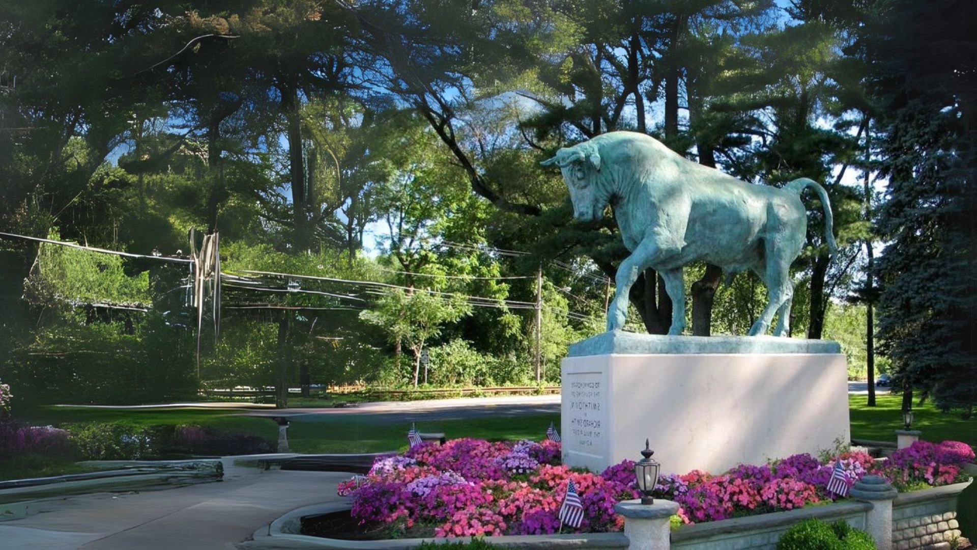 A statue of a bull surrounded by vibrant flowers in a lush, green park setting.