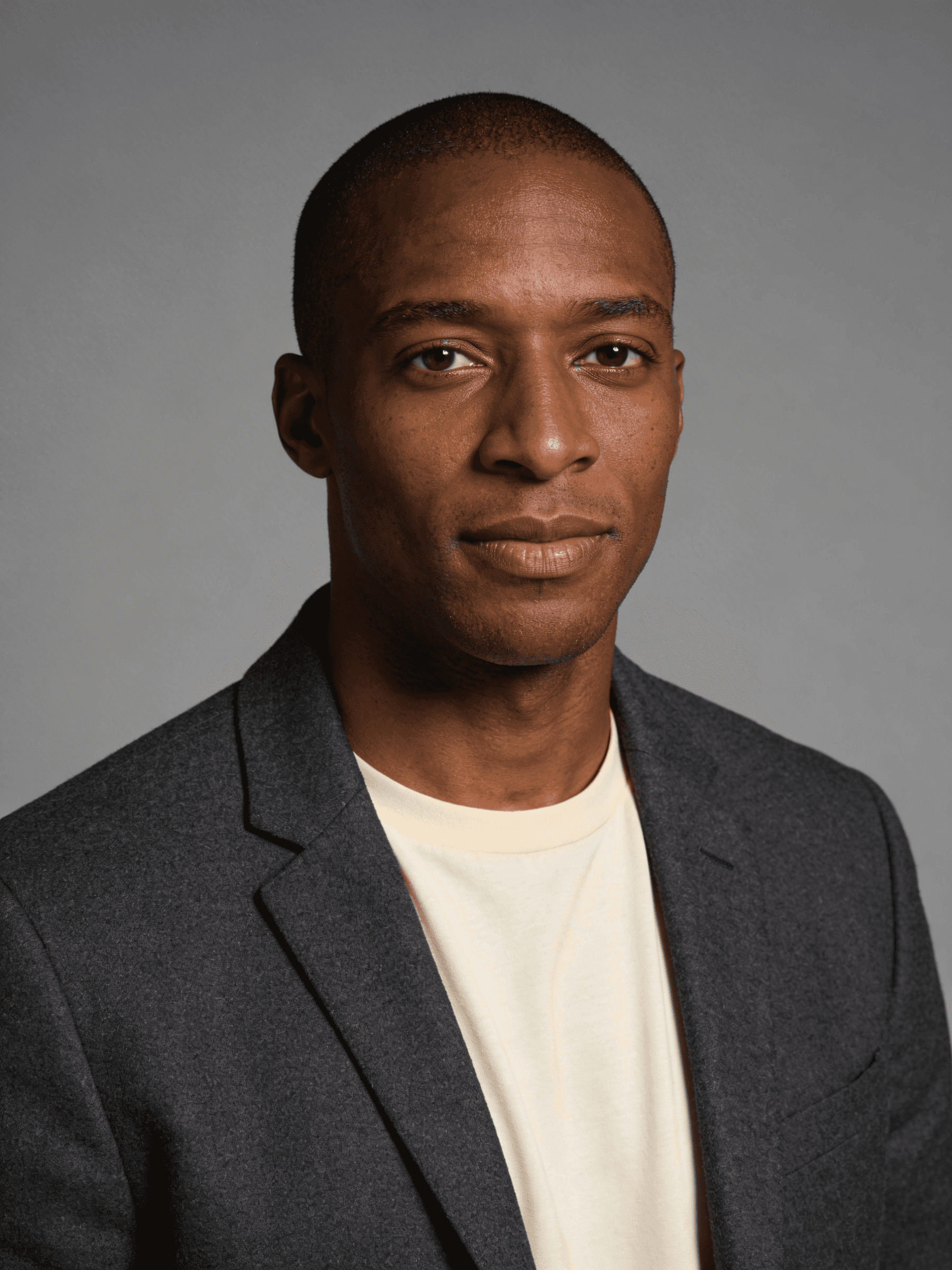 Portrait of a man in a gray blazer and light shirt, with a neutral background, creating a professional and focused look.
