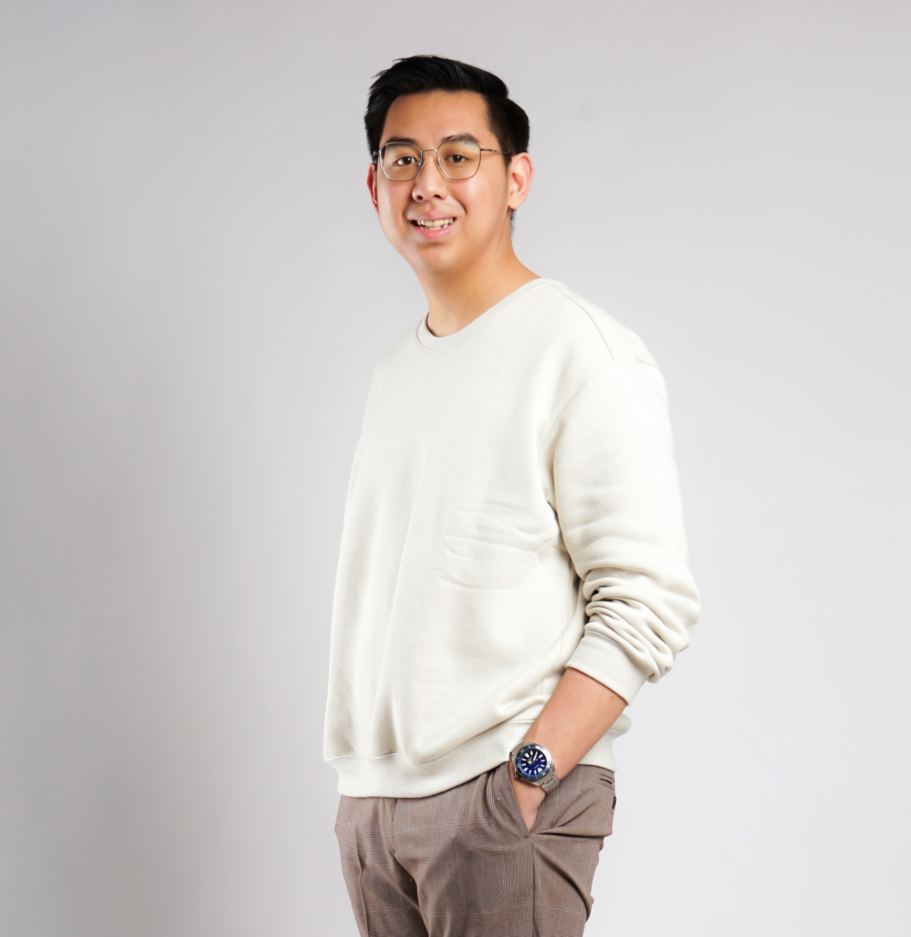 Asian man with glasses in a creative workspace, surrounded by colorful abstract art and stationery on a cluttered desk.