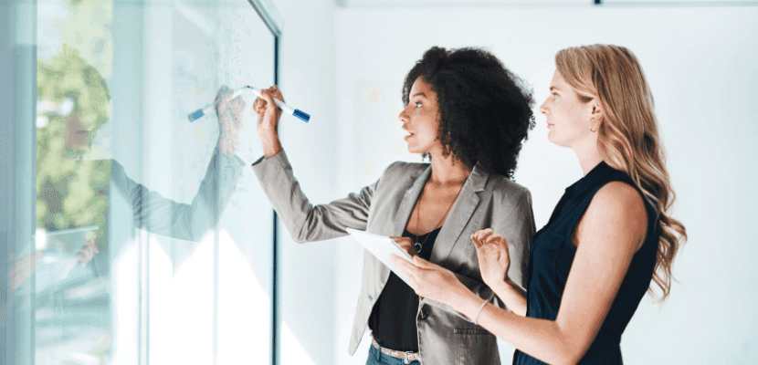 Two female professionals strategising at whiteboard