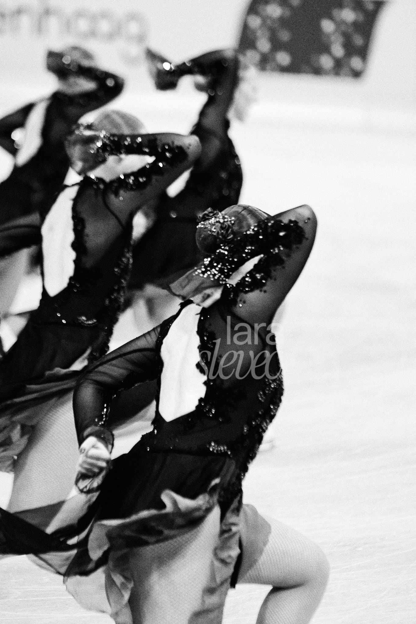 Schwarz-Weiß Bild mit vier Synchroneiskunstläuferinnen, die ihren rechten Arm gebeugt neben dem Kopf halten und die linke Faust hinter ihrem unteren Rücken. Team Helsinki Rockettes. ISU Synchronized Skating Championships 2026 in Salzburg. Fotografiert von Lara Slevec.