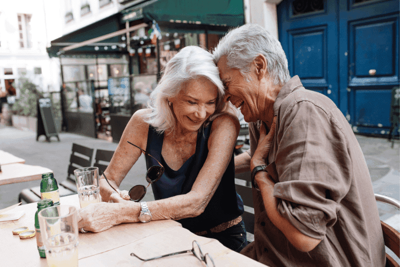 Senior couple laughing together at a Paris cafe terrace, illustrating retirement life in France