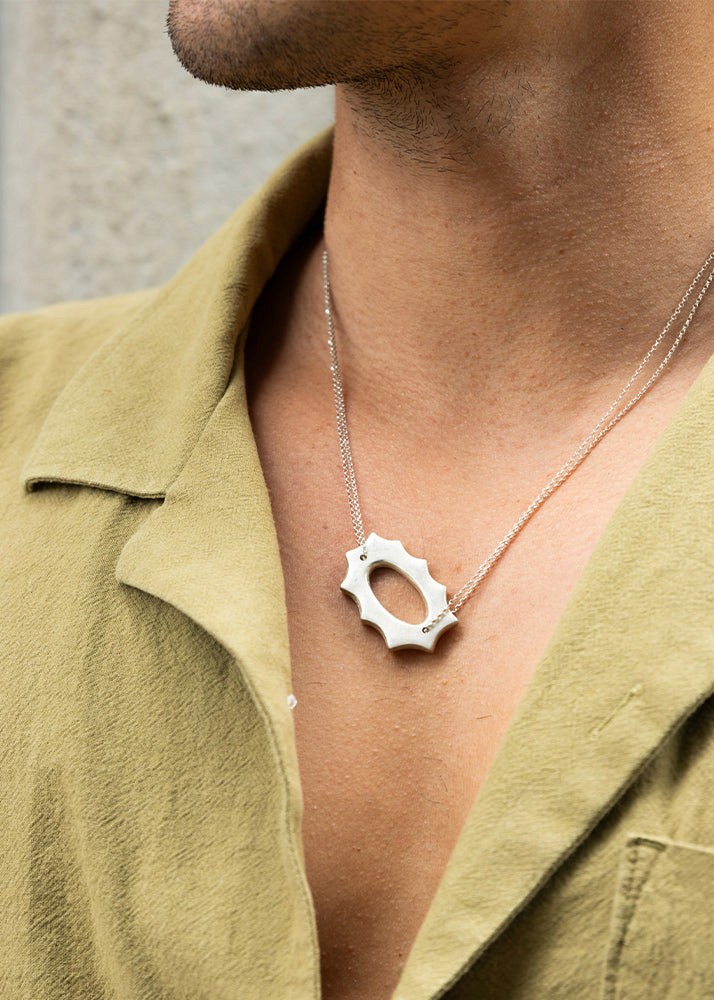 Person wearing a silver necklace with a unique pendant against a neutral background