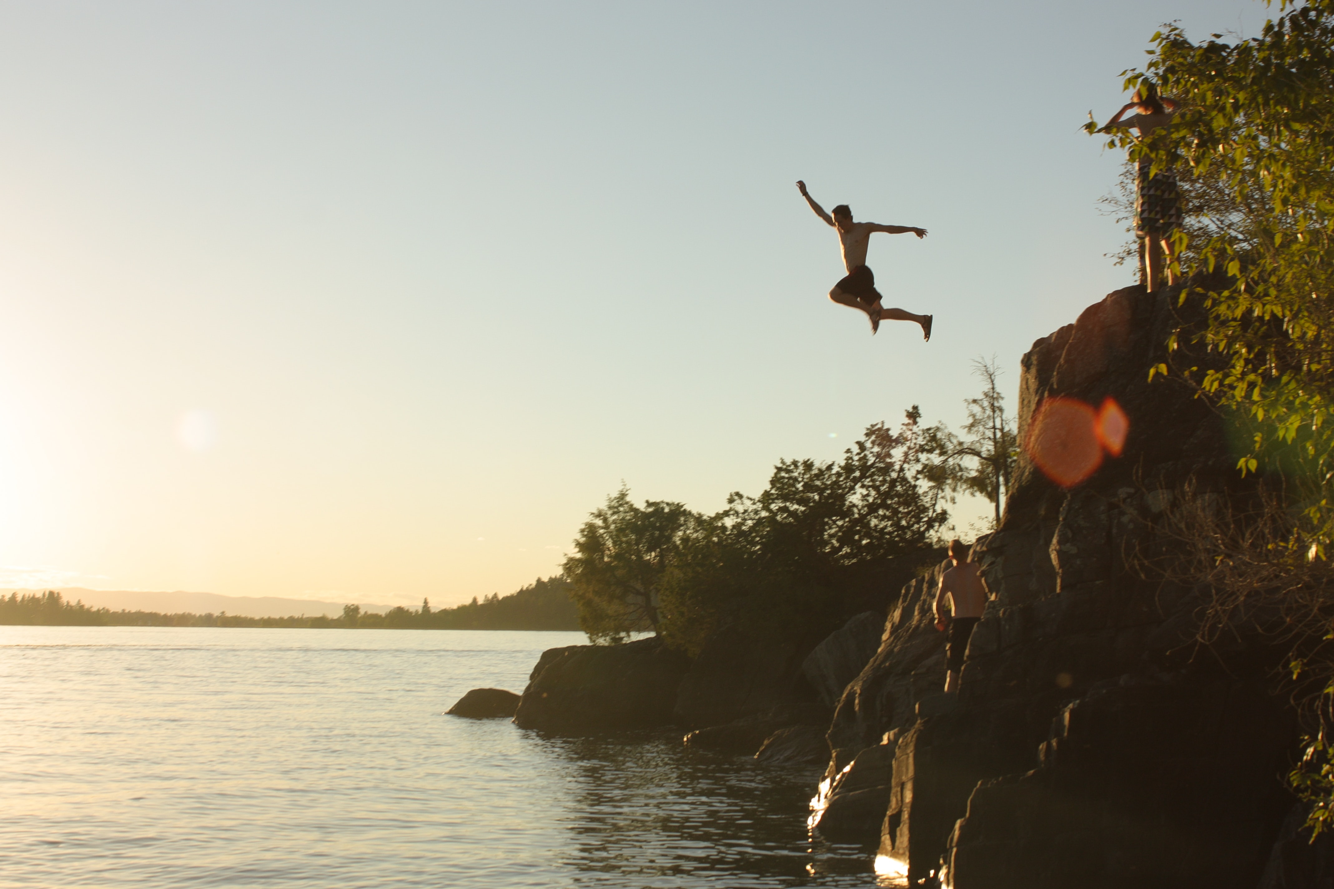 Person cliff jumping into a lake at sunset, symbolizing the bold action to discover a high-value brand partner ready to help you reach your creative marketing goals.