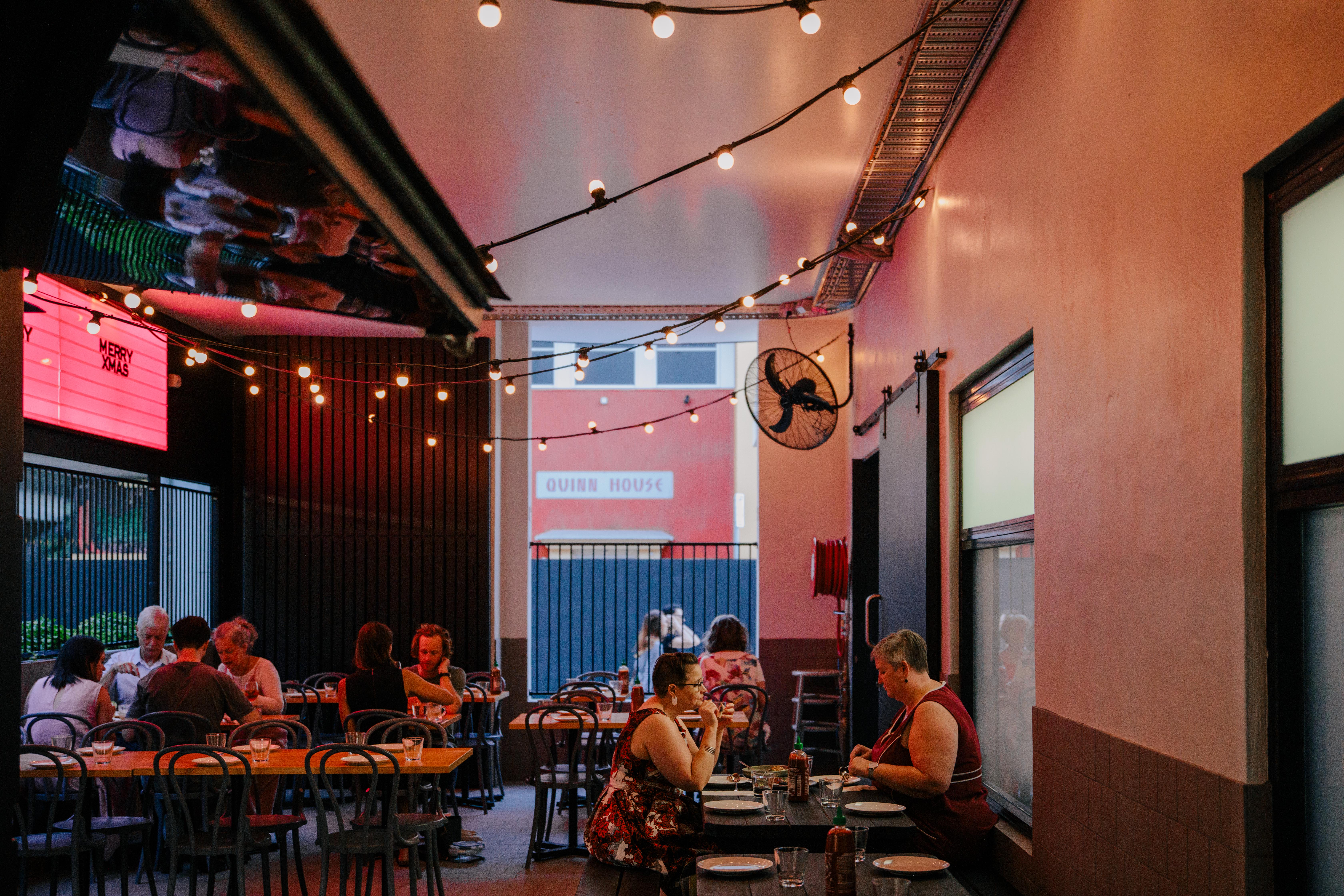 Laneway dining area at Hello Please, where string lighting, communal tables, and an open-air setting extend the restaurant into the surrounding urban context.