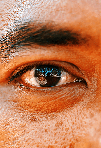 Smiling young woman with long hair standing against a dark green background, holding a finger to her chin.