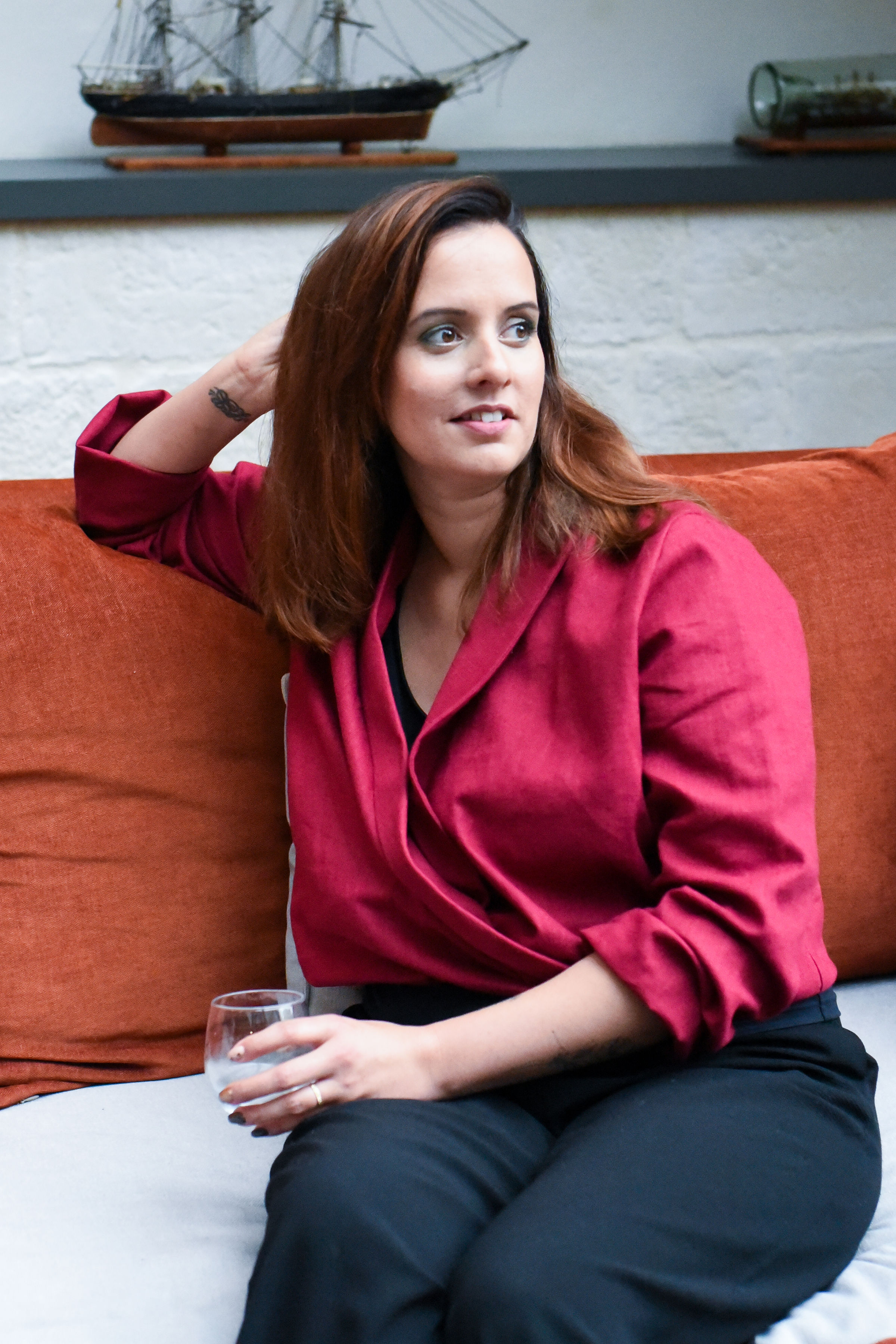 Femme accoudée sur un divan, le regard porté au loin, incarnant une douceur confiante. Elle porte le chemisier d’allaitement Framboise, version « l’Éclatante », dont la teinte vibrante met en lumière toute sa féminité. Une coupe pensée pour les jeunes mamans, alliant style, confort et praticité, tout en célébrant l’éclat naturel de la maternité.