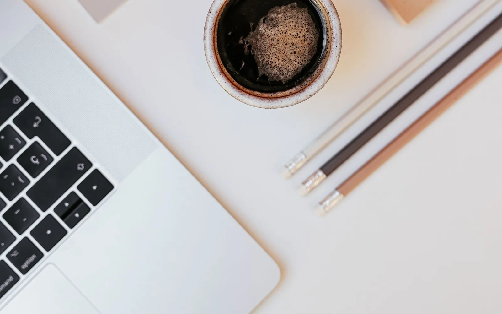 A cup of coffee, a laptop and pencils on a white desk, seen from above