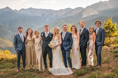 The couple pose with a group of wedding guests against the mountain panorama.