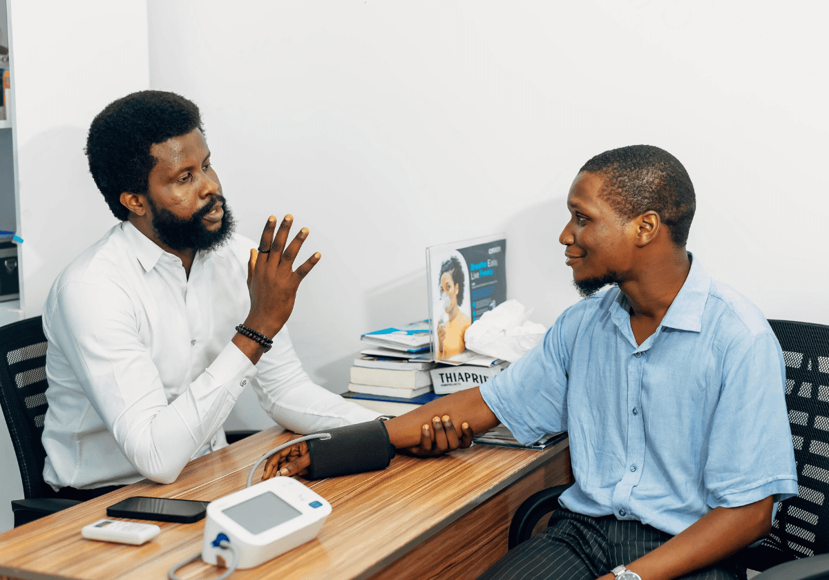 A smiling young man with crossed arms, wearing a plaid shirt and white t-shirt, poses against a dark background.