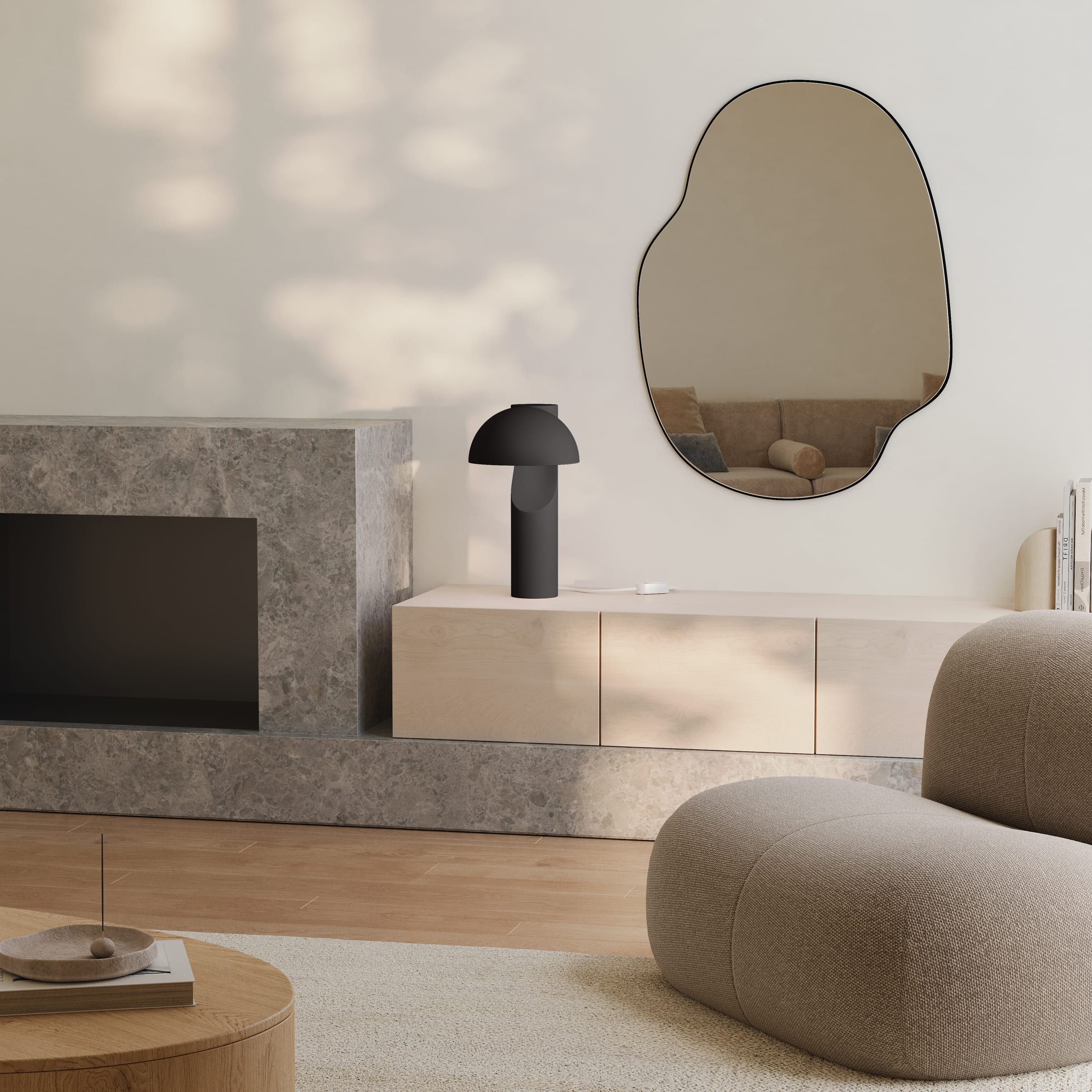 Black table lamp with a dome shade on a pale wood console beside a stone fireplace, below an organic wall mirror