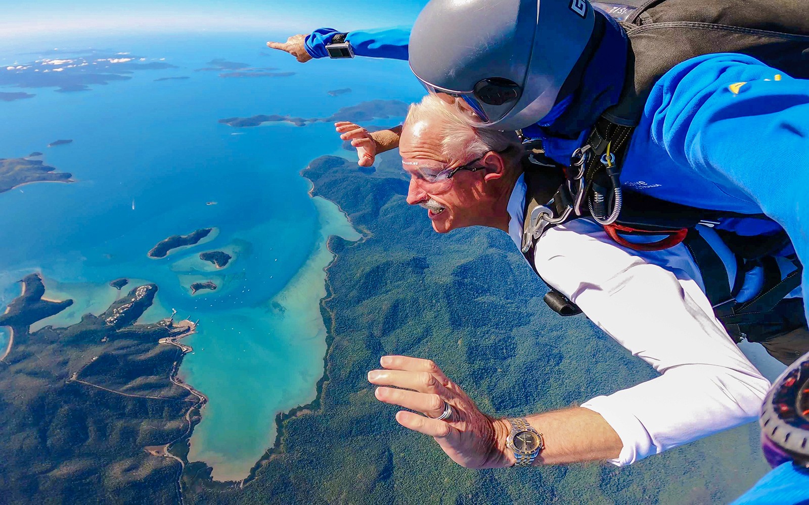 צניחה חופשית בצניחה זוגית מעל קו החוף של חוף איירלי, קווינסלנד, עם אוקיינוס תוסס ונוף ירוק מתחת.