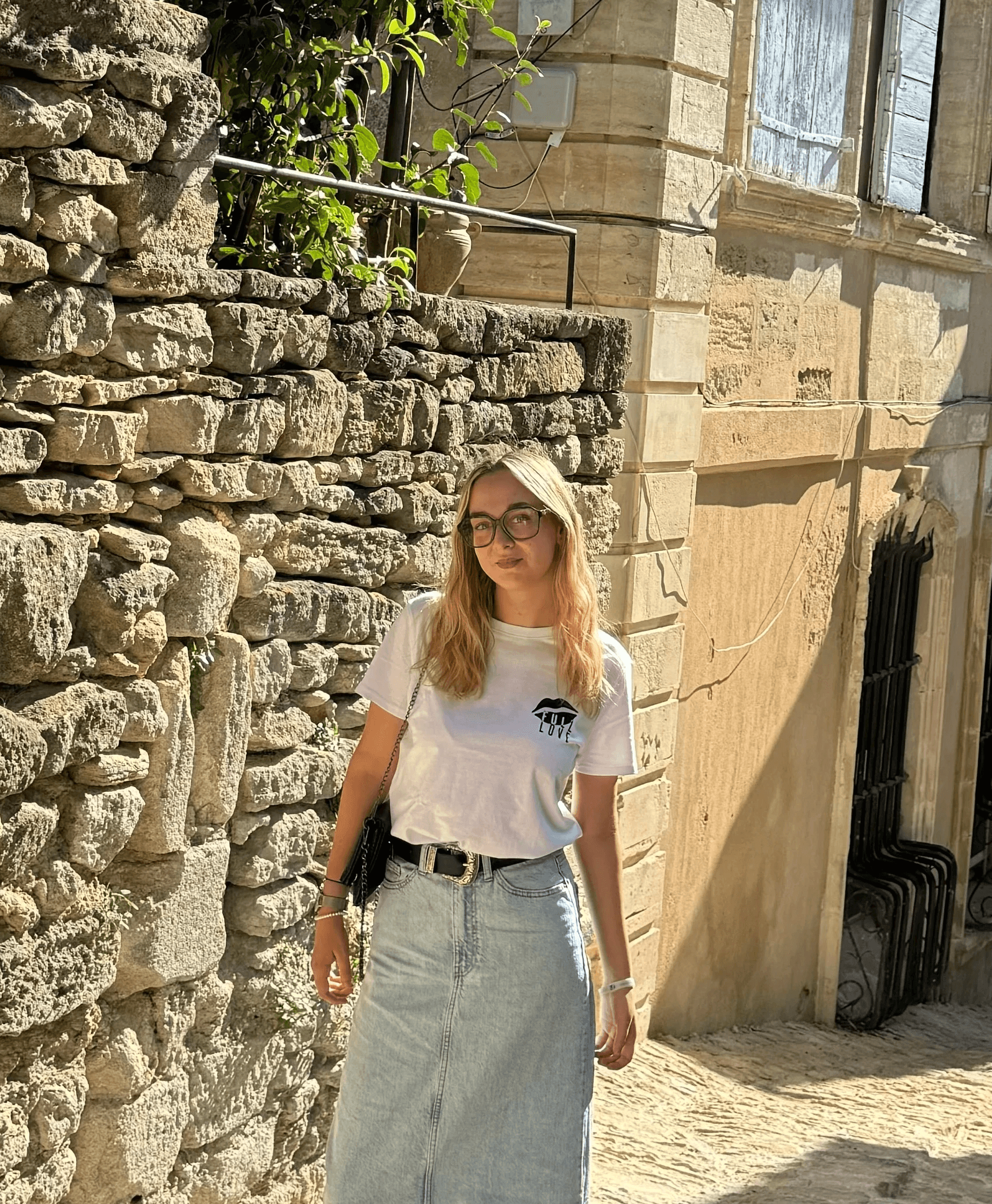 Femme blonde en lunettes et t-shirt blanc dans une ruelle en pierre, portrait de voyage