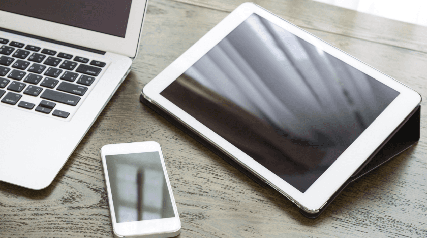 A sleek workspace featuring a laptop, tablet, and smartphone placed on a wooden desk, highlighting modern technology and connectivity.