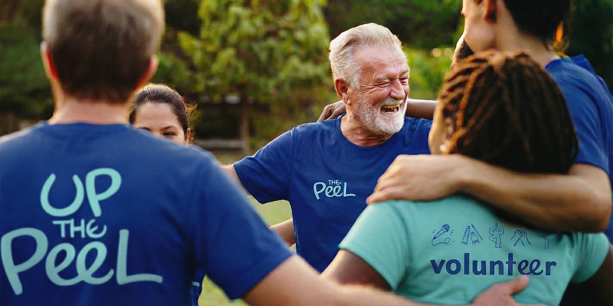 Group of volunteers for The Peel Institute standing in a circle with arms around eachother