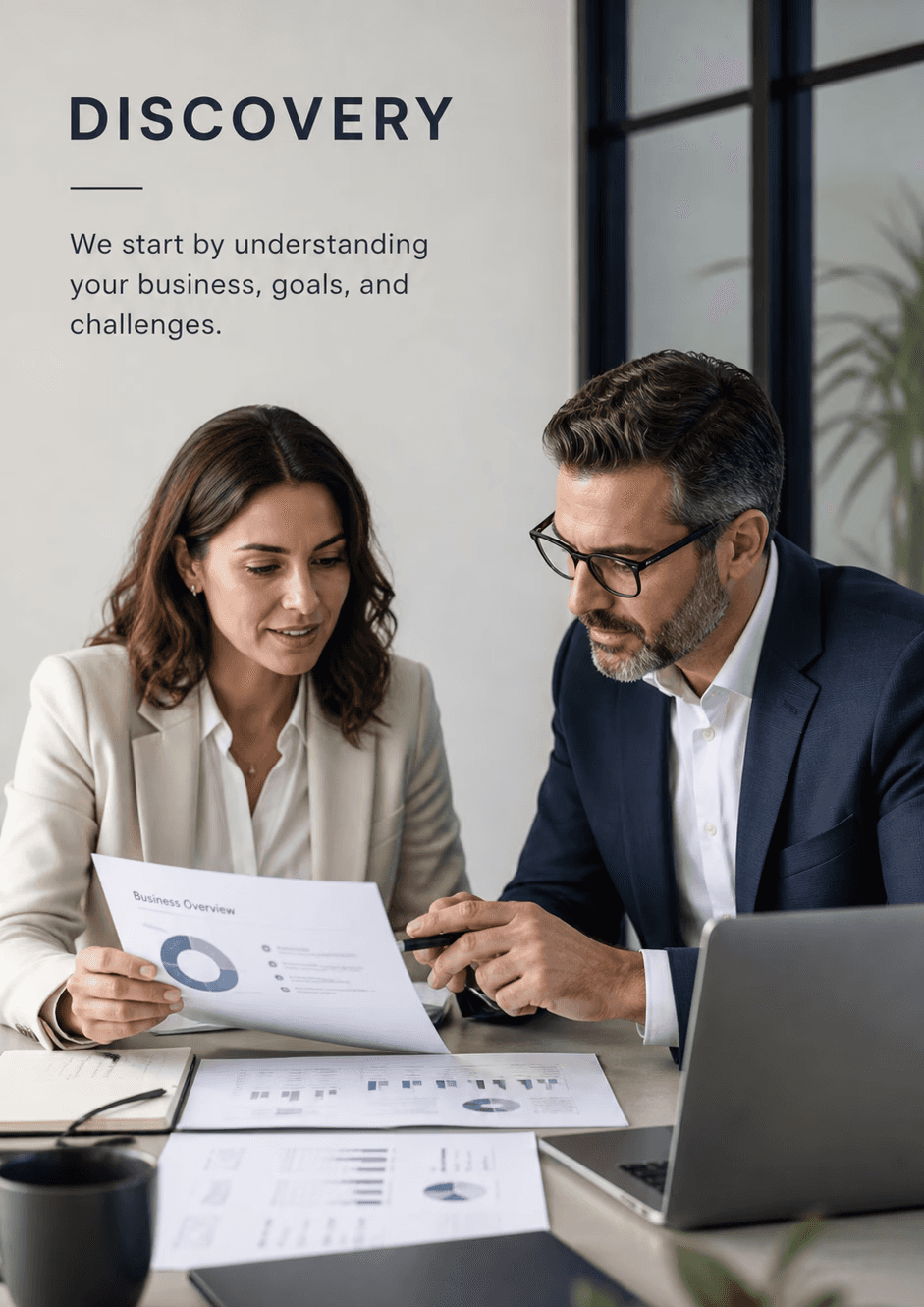 Two professionals reviewing documents at a table in a modern office, discussing business challenges and goals, with a clean workspace and neutral background, vertical layout for website hero section.