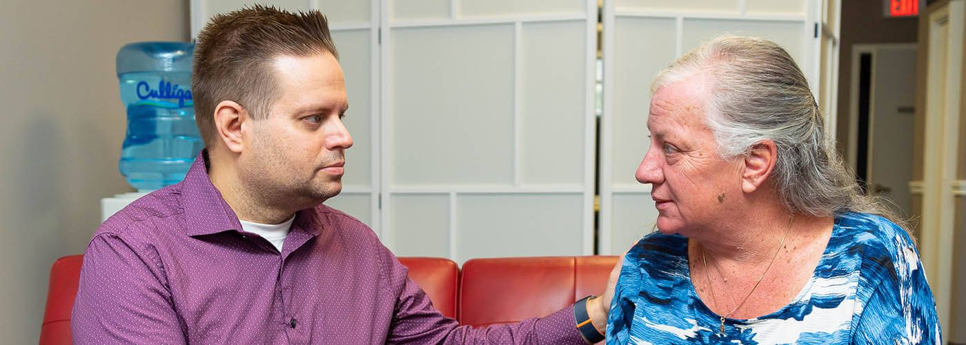 A young man and an older woman sit across from each other, engaged in a serious conversation indoors.