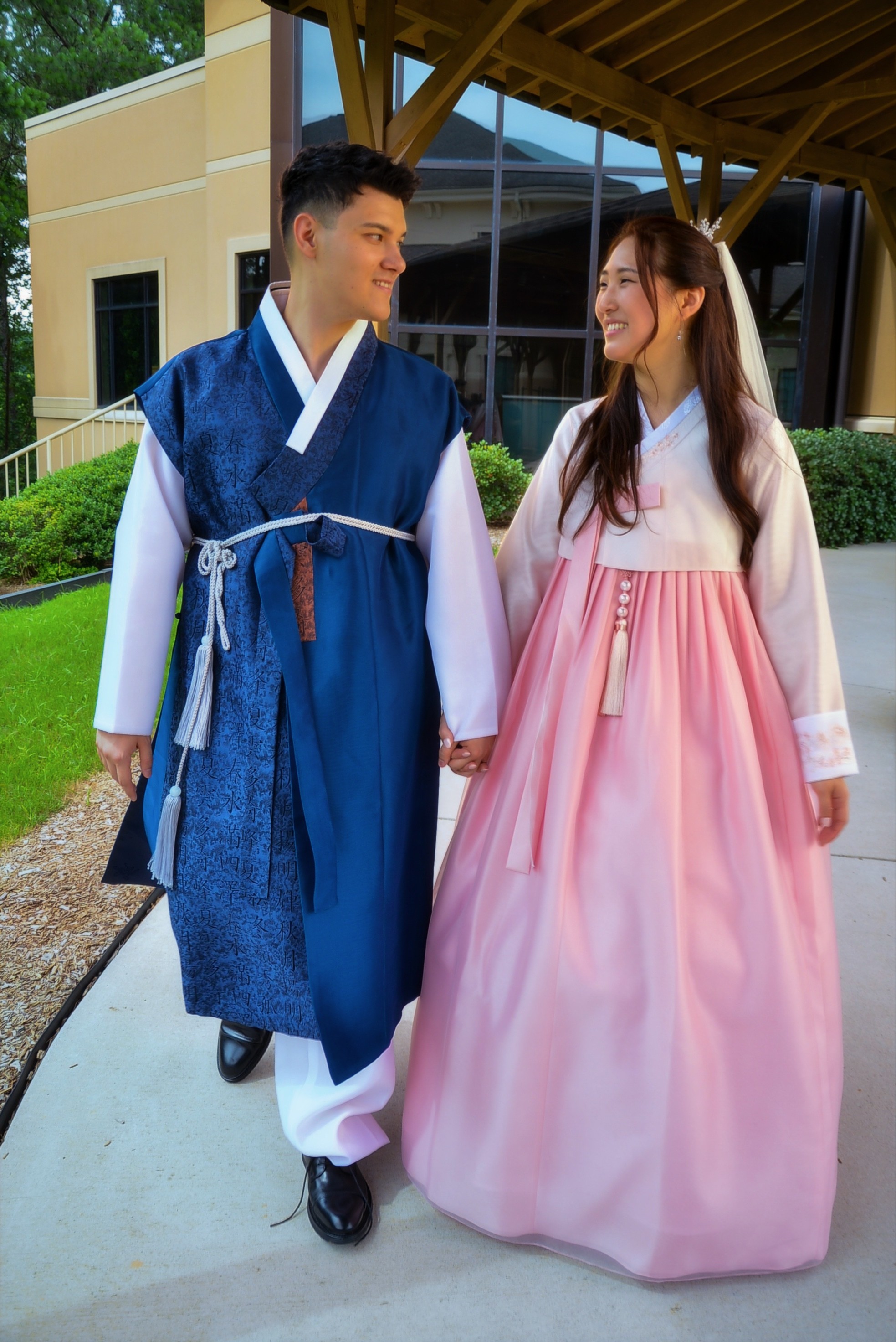 Bride and groom walking hand in hand in pink and blue hanbok outside Korean Church of Atlanta, Duluth GA
