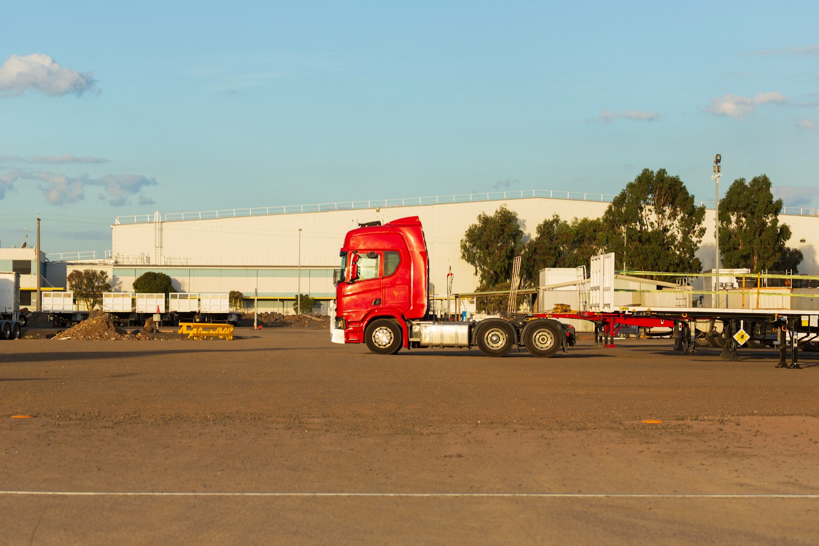 A red lorry with a flatbed trailer parked outside a large distribution warehouse