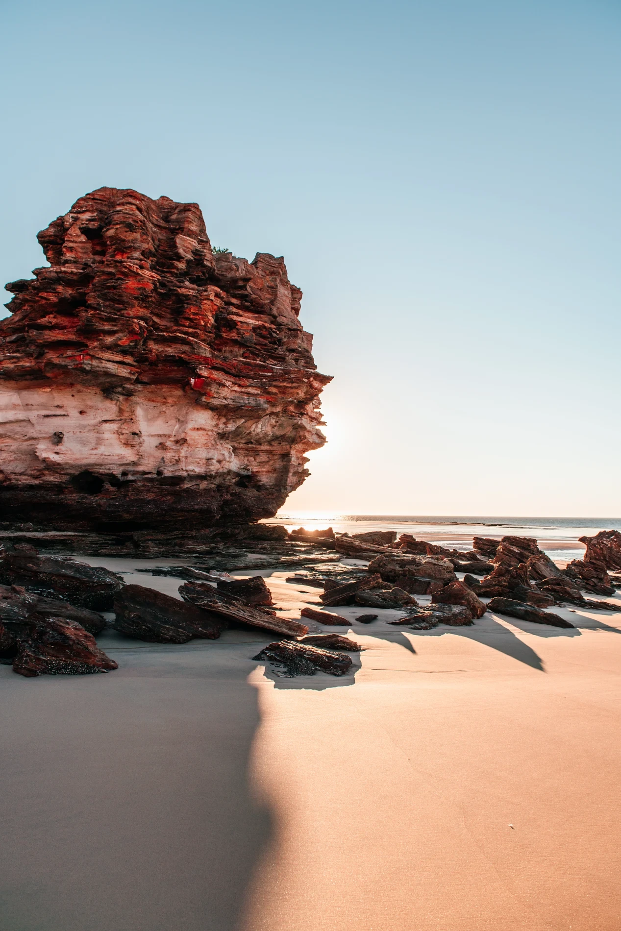 A red sandstone sea stack on a wet beach, backlit by low sun