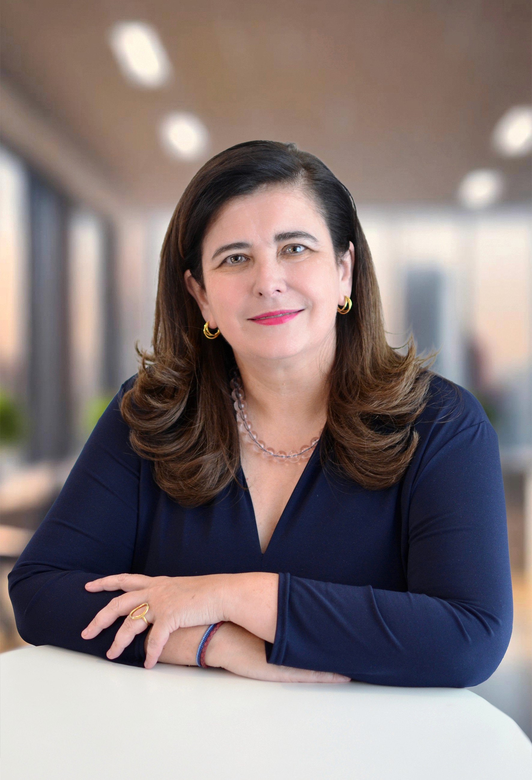Una persona sonriente con cabello rizado, vistiendo una chaqueta de cuero, se encuentra en un acogedor espacio interior.