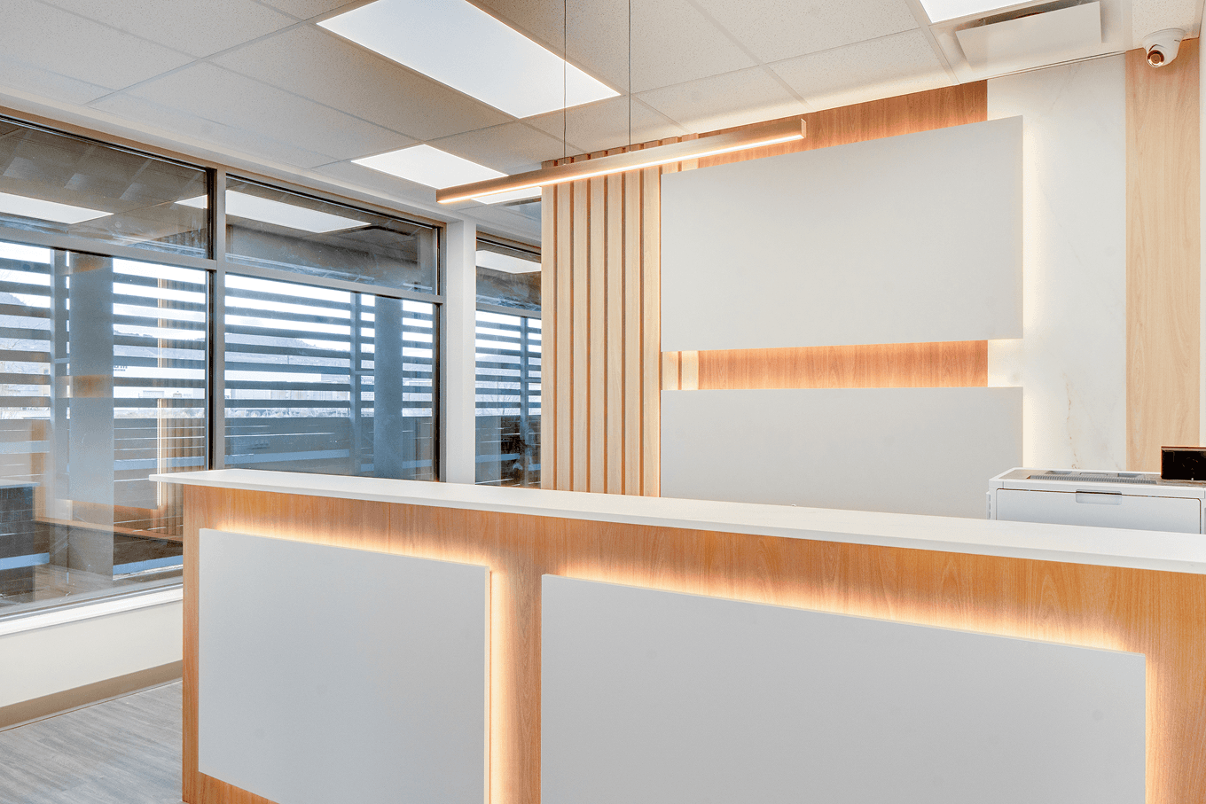 Reception desk and feature wall with integrated lighting, wood slats, and large decorative panels in a bright commercial lobby.