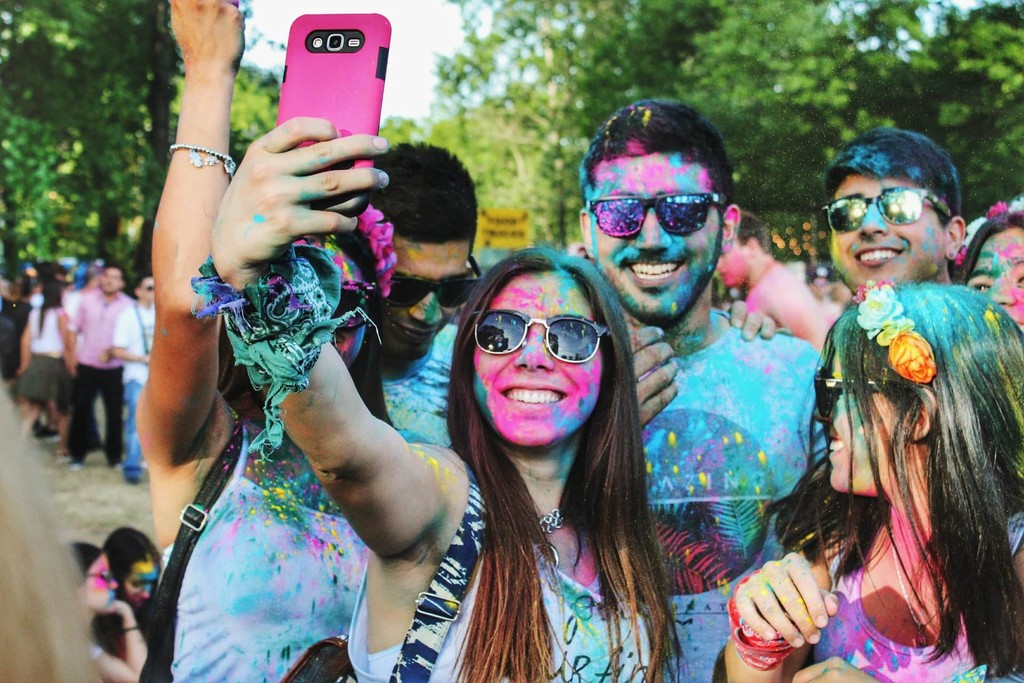 Group taking colorful selfie during Holi festival, celebrating with vibrant powder.