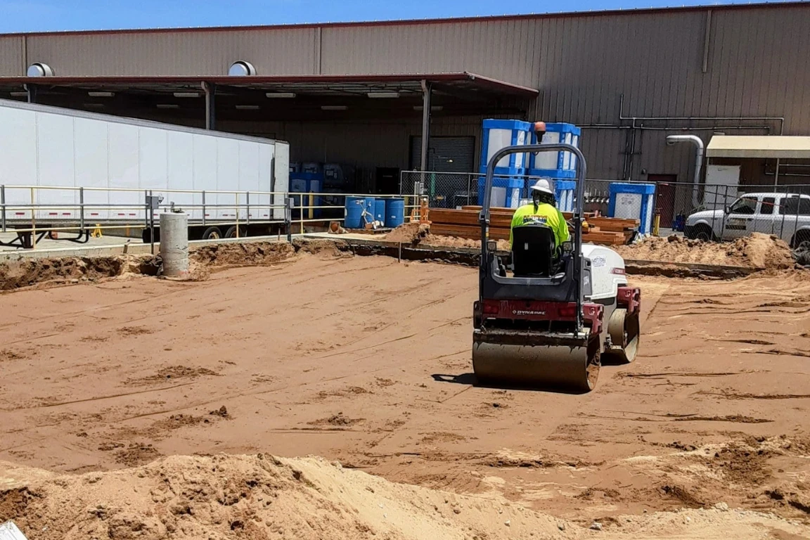 Tractor from John Alonso Concrete loading broken concrete and dirt for haul‑off at an industrial property.