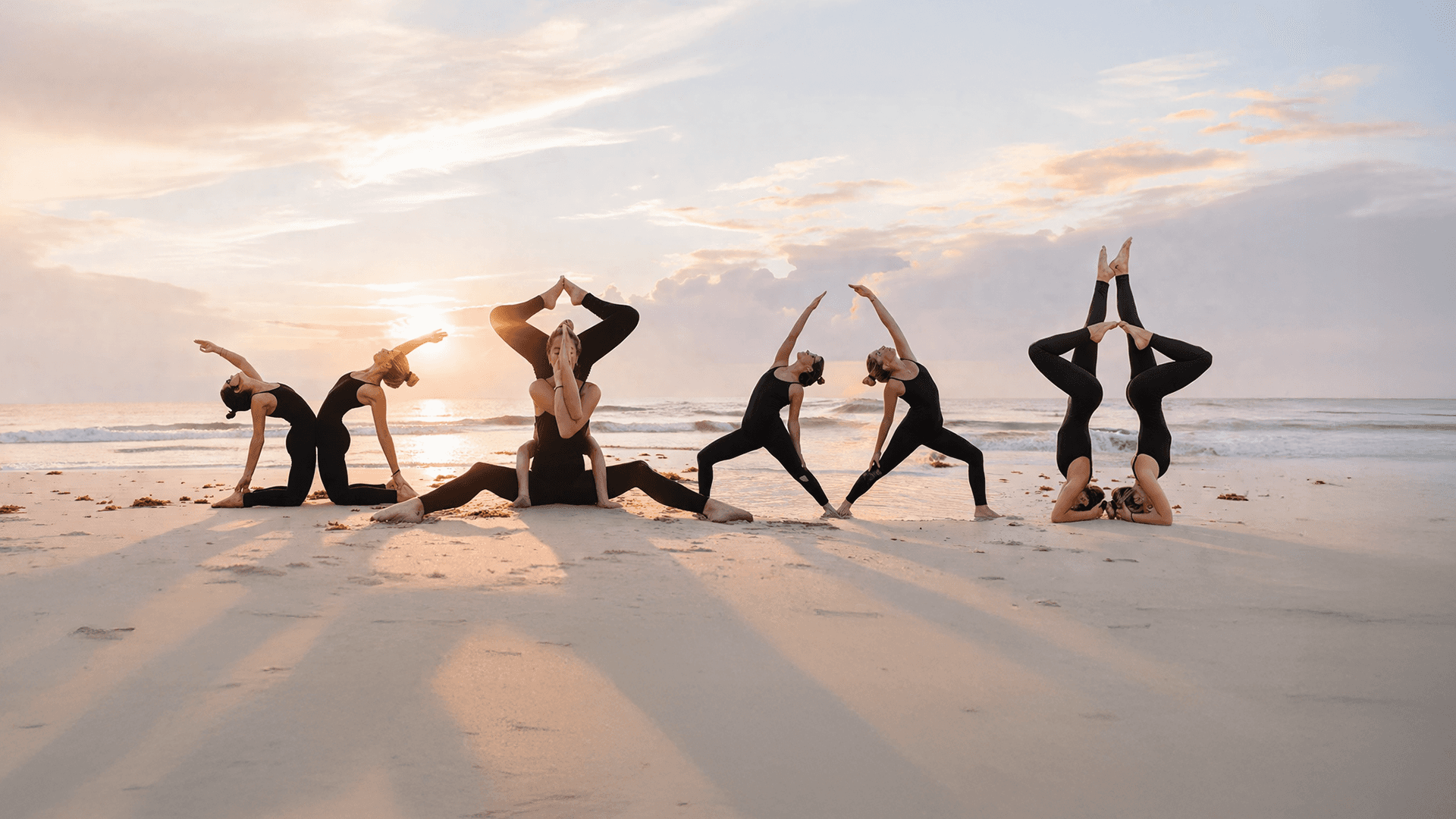 Group of women practicing yoga poses on the beach at sunset wearing Treelance organic cotton yoga apparel