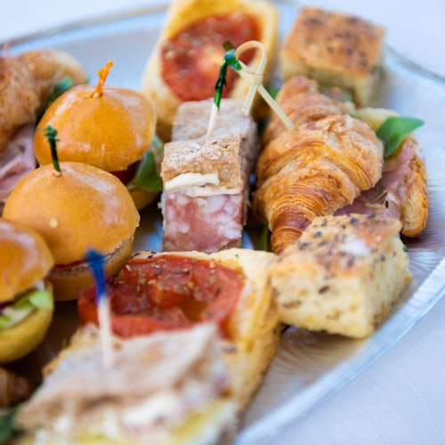 A tray of assorted finger foods including small sandwiches, croissants, and focaccia with toothpicks holding some items together.