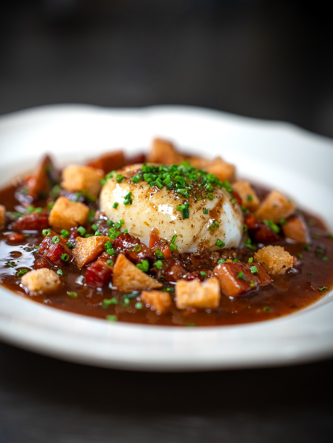 Gourmet dish plated in a black bowl on a dark wooden table.