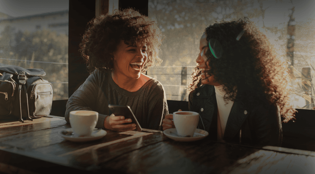 Two colleagues laughing with eachother whilst drinking coffee