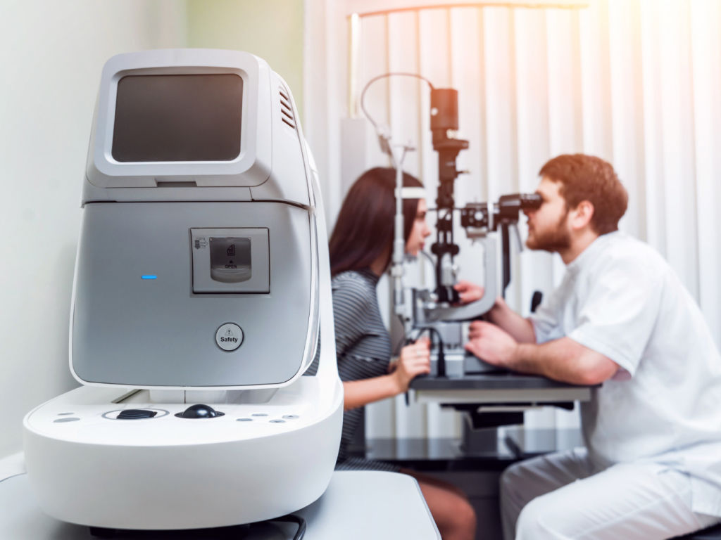 A male doctor examining a woman in an eye exam machine to assess their vision.