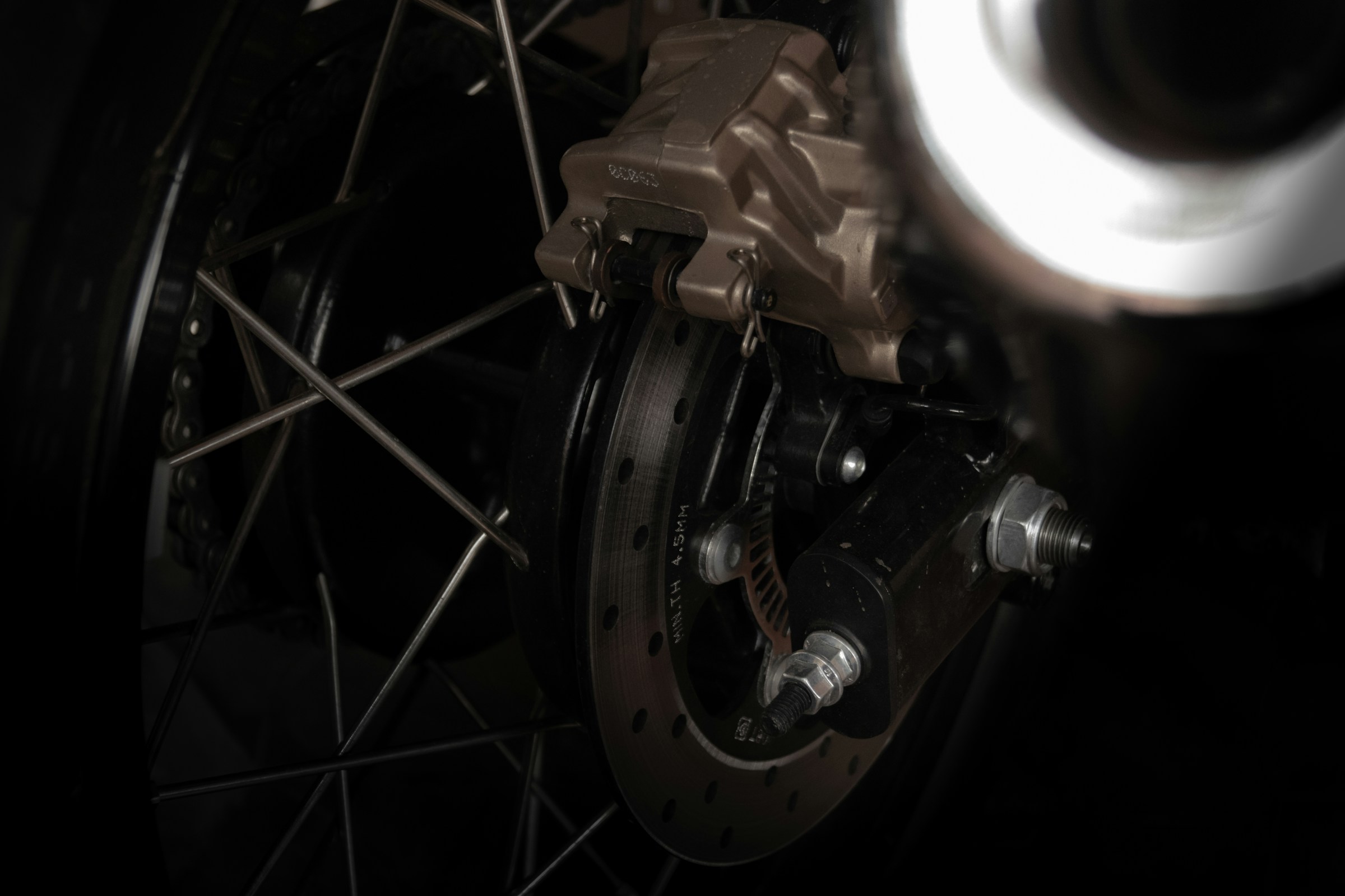 A spoked motorcycle wheel and brake caliper in the dark