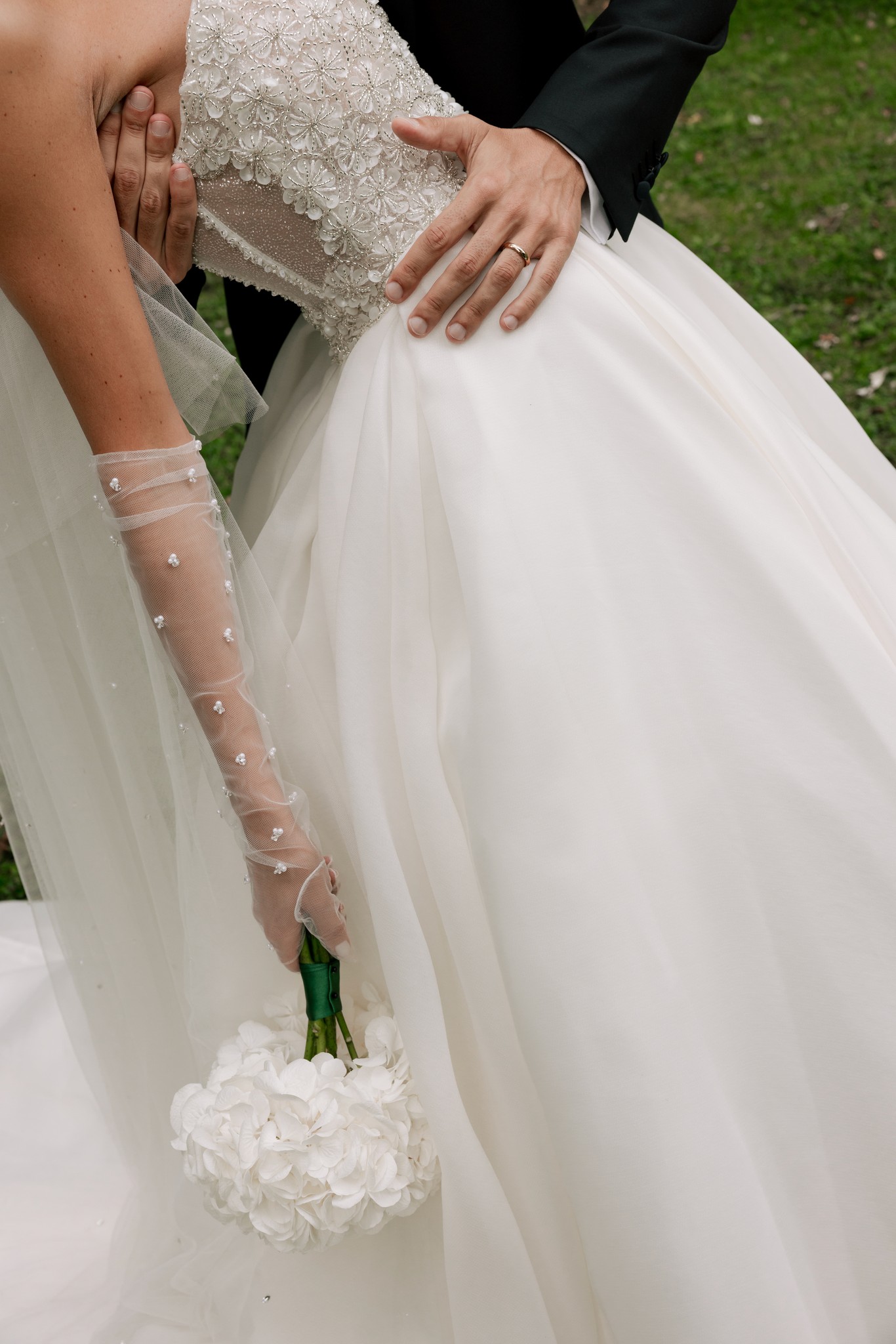 Sposa in abito bianco con velo ricamato a perle stringe il bouquet di ortensie, sposo accanto a Villa Ferrari