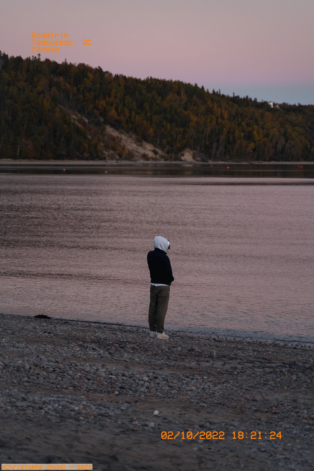 Promeneur en bord de l'eau à Tadoussac sous un ciel de fin de journée.