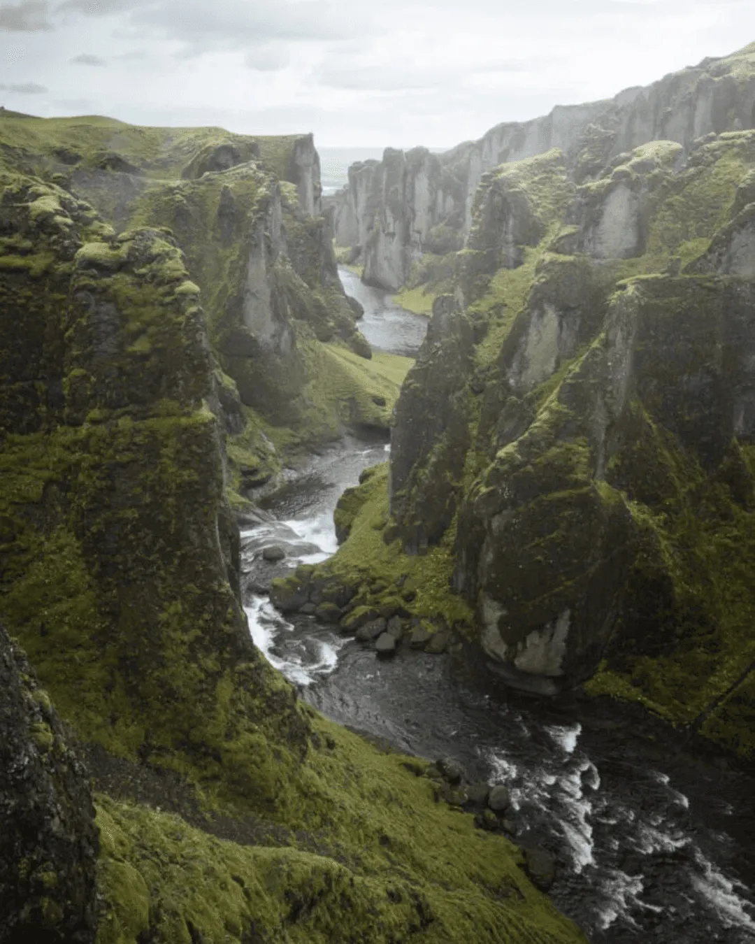 A deep, winding river canyon with steep, moss-covered green cliffs at Fjaðrárgljúfur, Iceland