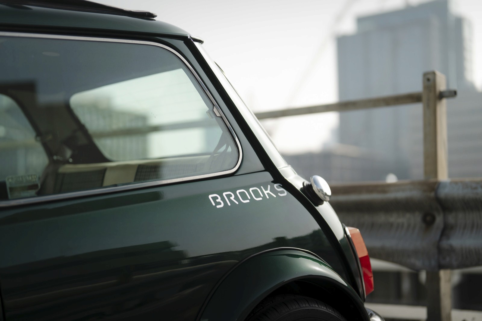 A close-up of a green car's rear panel, with a city skyline visible in the blurred background.