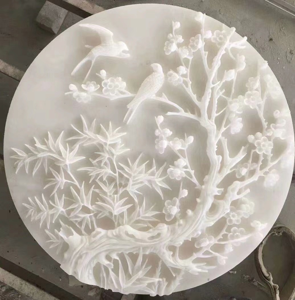 A circular white marble carving featuring birds and flowers in a nature-inspired design.