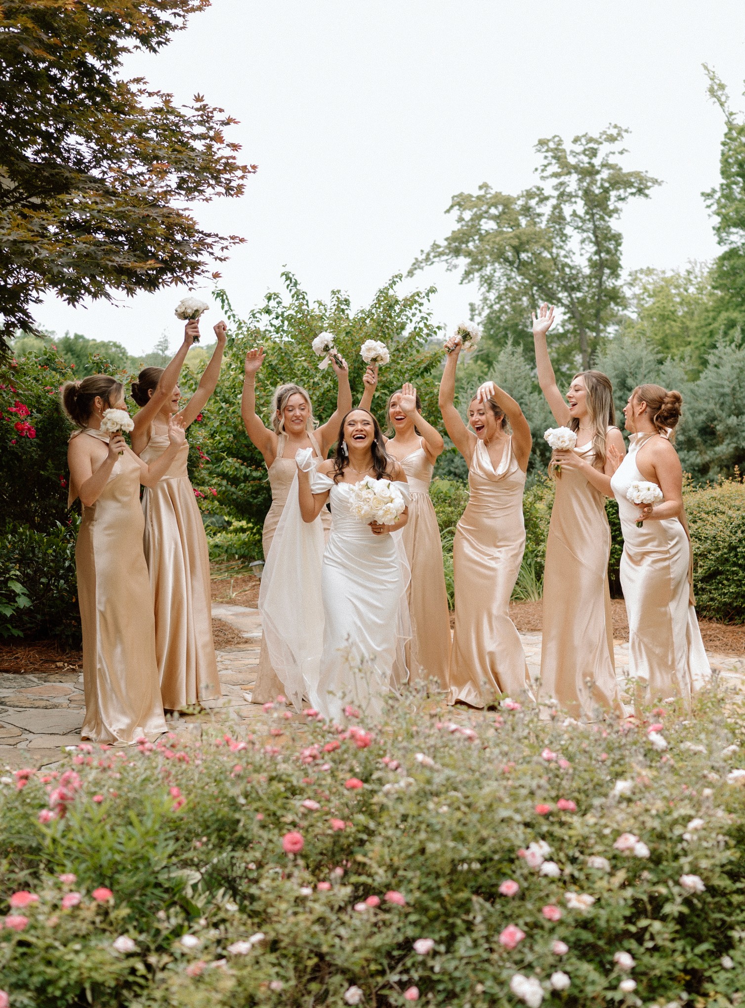 Ally and her bridesmaids raise bouquets and cheer in the garden.