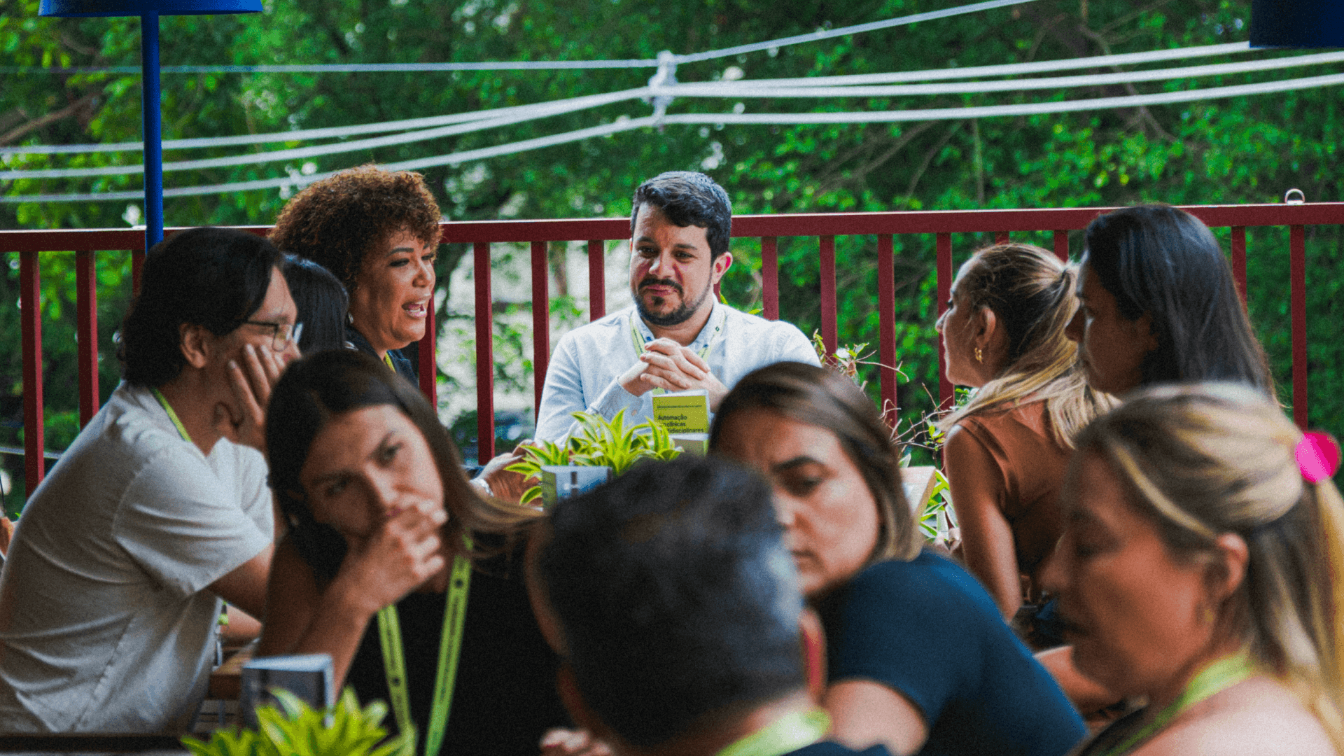Grupo de participantes reunido em mesas durante encontro da Tivita com representantes de clínicas, em ambiente aberto e arborizado, conversando de forma descontraída durante o evento realizado na Dengo, em São Paulo.