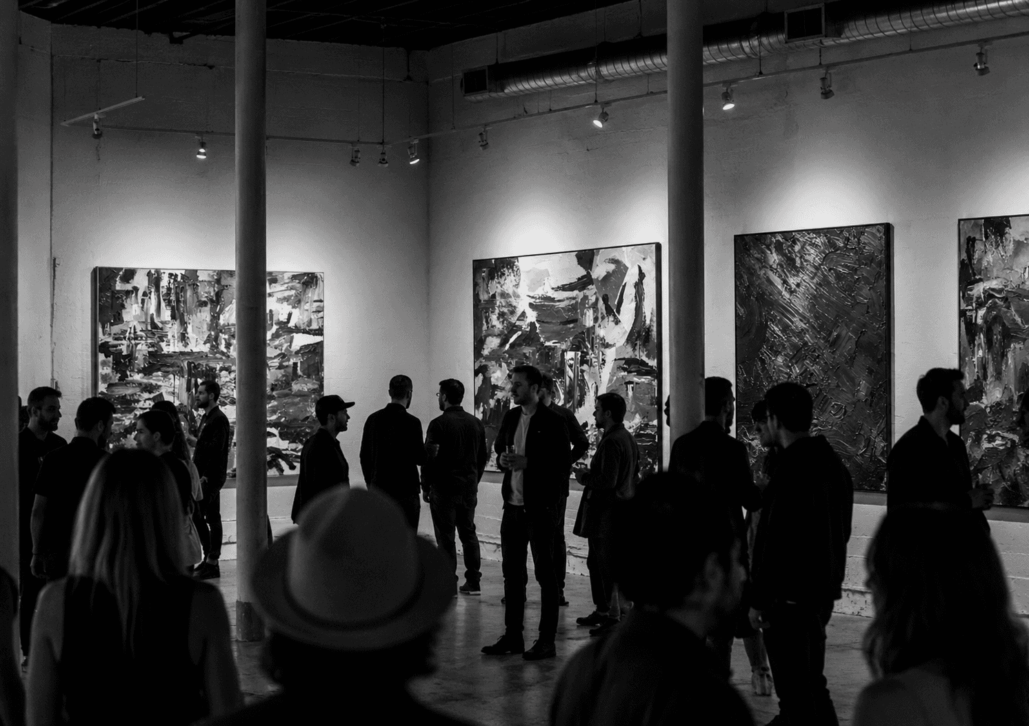 A crowded black-and-white art exhibition with abstract paintings on the walls