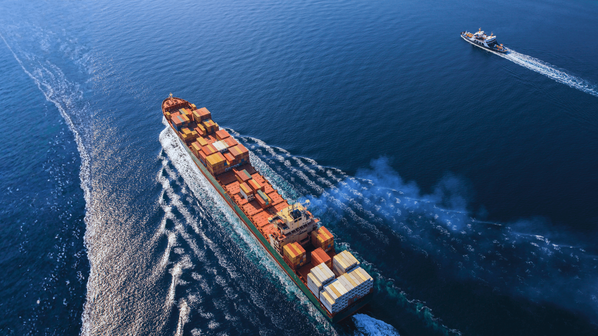 A young person with curly hair smiles at the camera while sitting in front of a laptop against a dark background.
